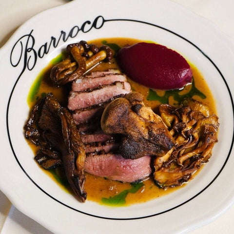 Plated dish with sliced meat, vegetables, and a red puree on a white plate with 'Barroco' branding.